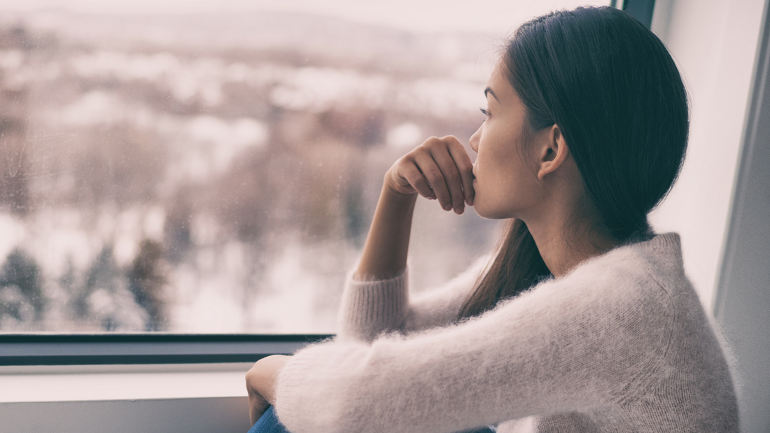 Woman in deep thought gazing out the window with a winter forest in the background.
