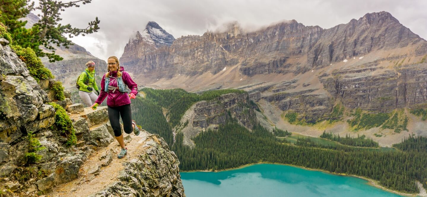 Women running on the edge of a cliff above a beautiful blue lake