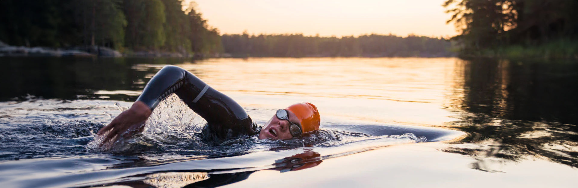 A swimmer in a lake wearing goggles, a swim cap, and a wetsuit